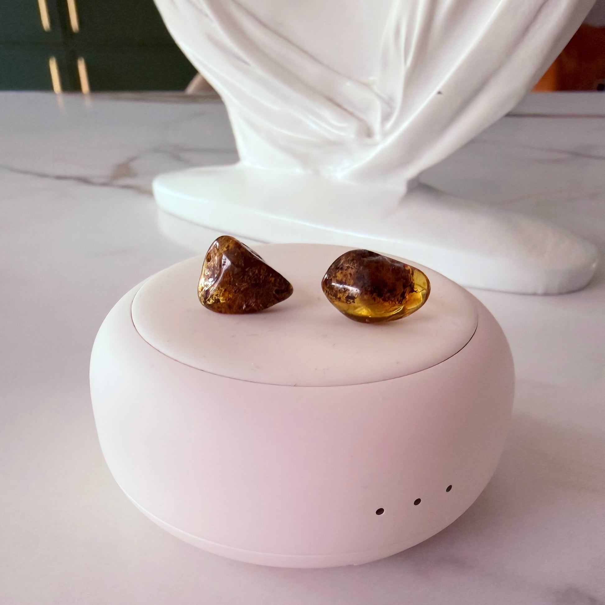 Pair of amber-colored earrings on a white spherical container with a decorative white base.