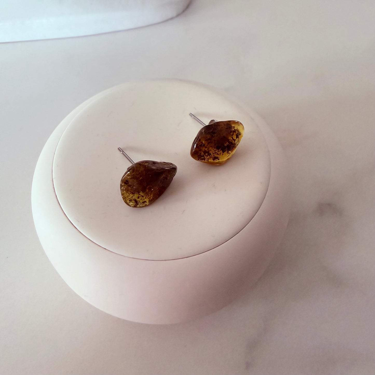 Teardrop-shaped amber earrings on a white circular stand with a marble background