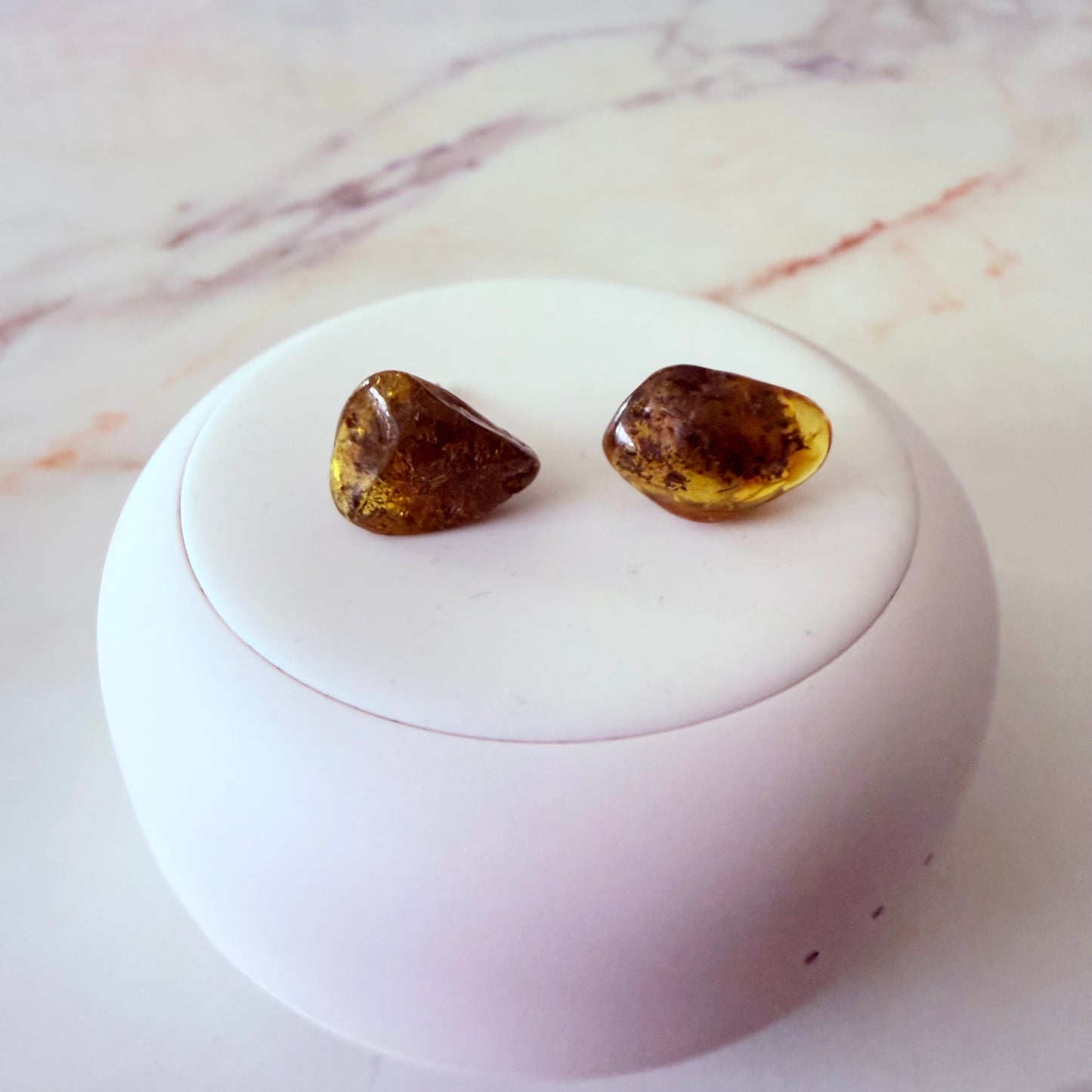 Pair of amber-colored earrings on a white round stand with a marble background