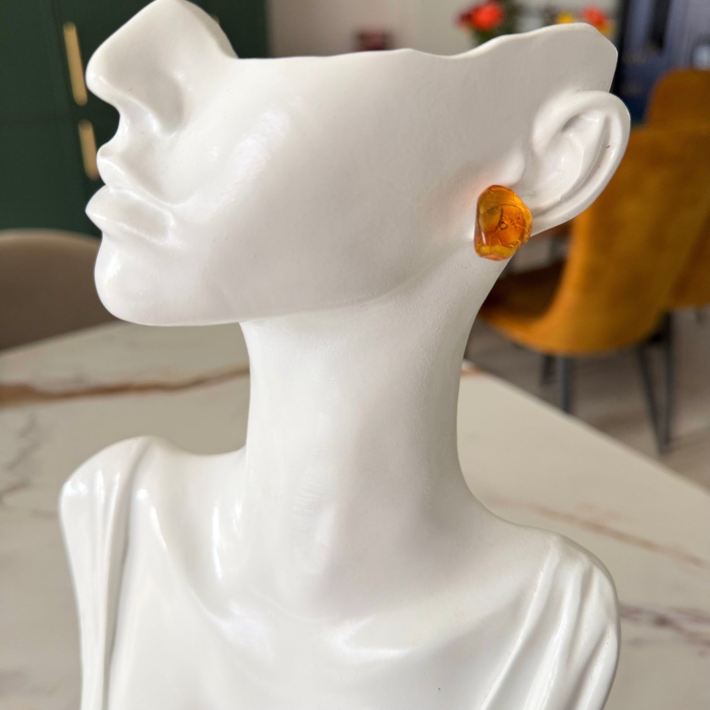 White marble bust with a yellow earring on a blurred indoor background