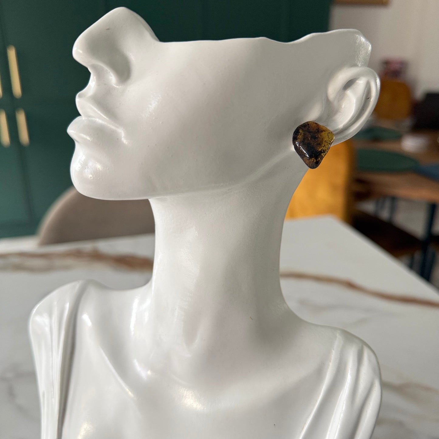 White ceramic bust with a yellow gemstone earring on a blurred indoor background