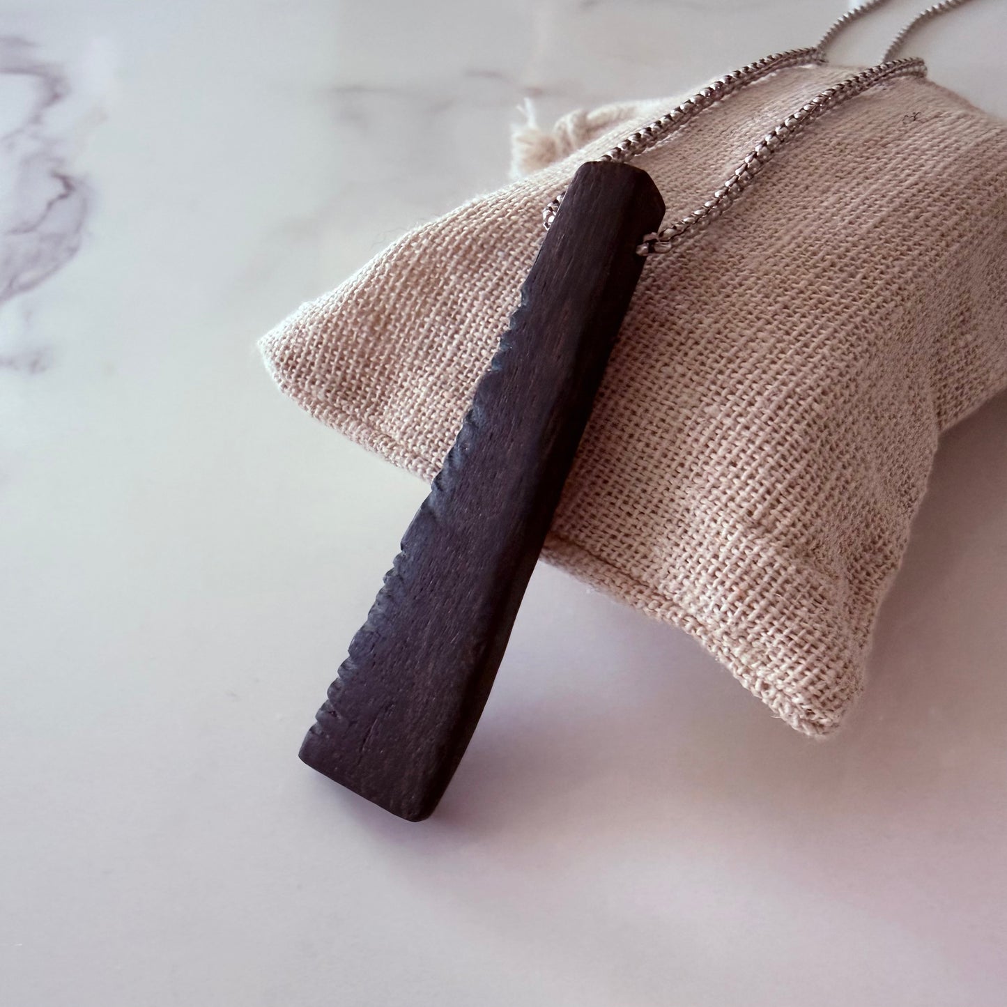 Dark wooden tool on a beige textured pouch against a marble background