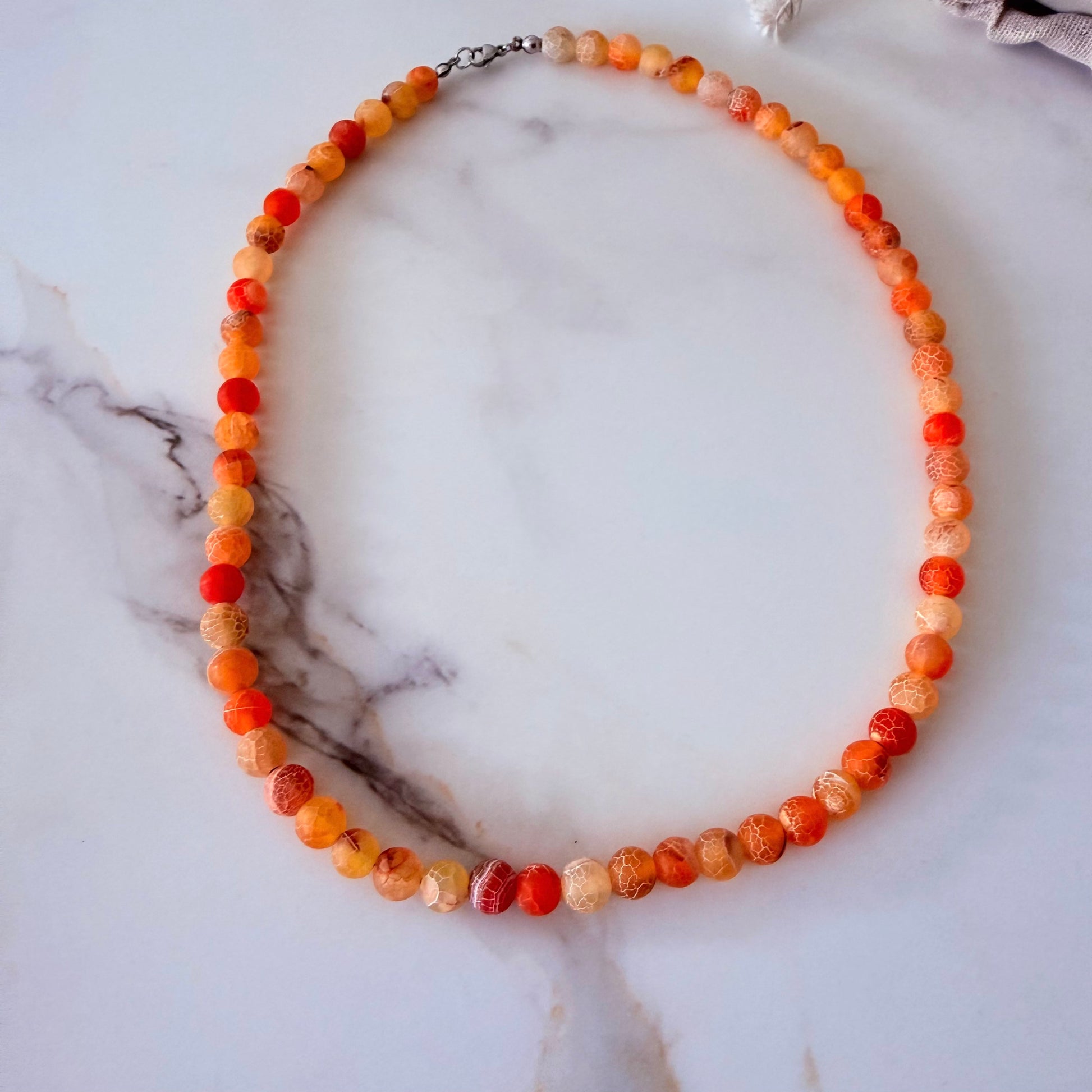 Necklace with orange and red beads on a marble surface
