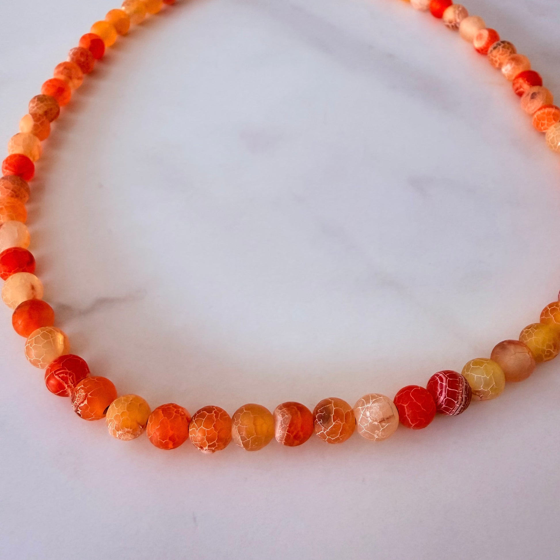 Necklace with agate orange and red beads on a white marble surface