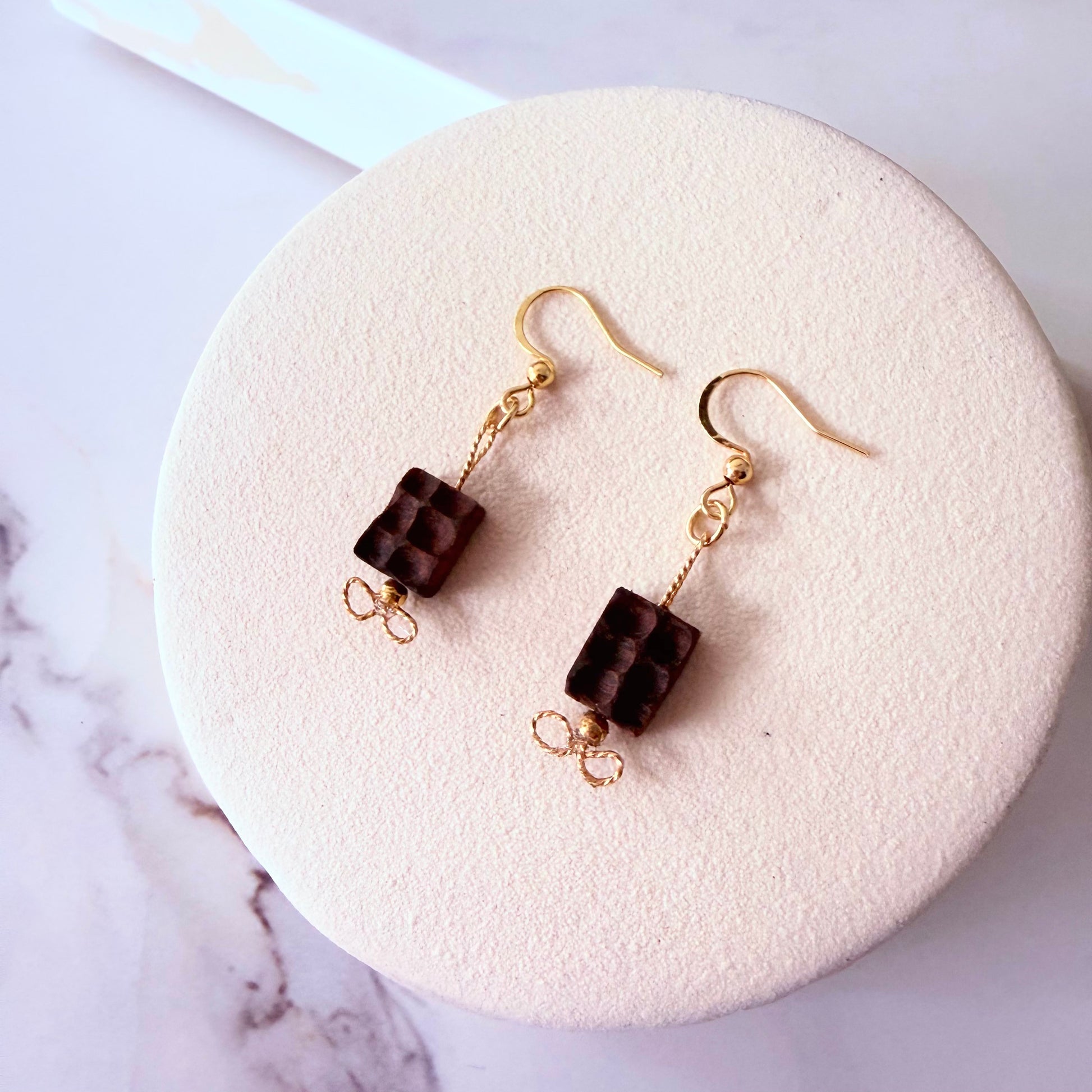 Pair of brown square bead earrings on a white stand with marble background