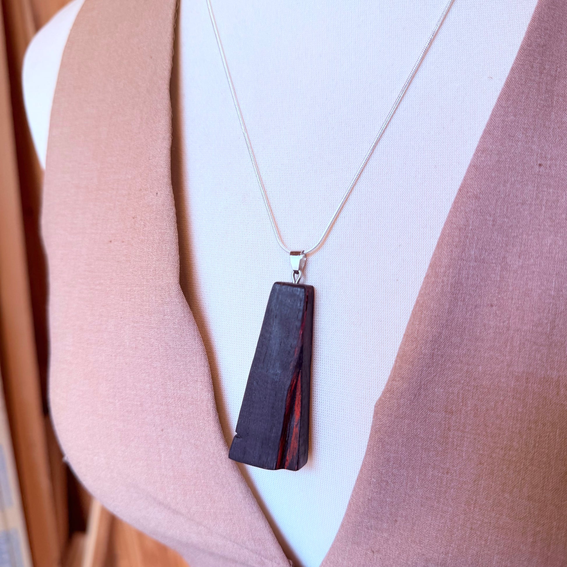 Necklace with a dark pendant worn by a person against a neutral background
