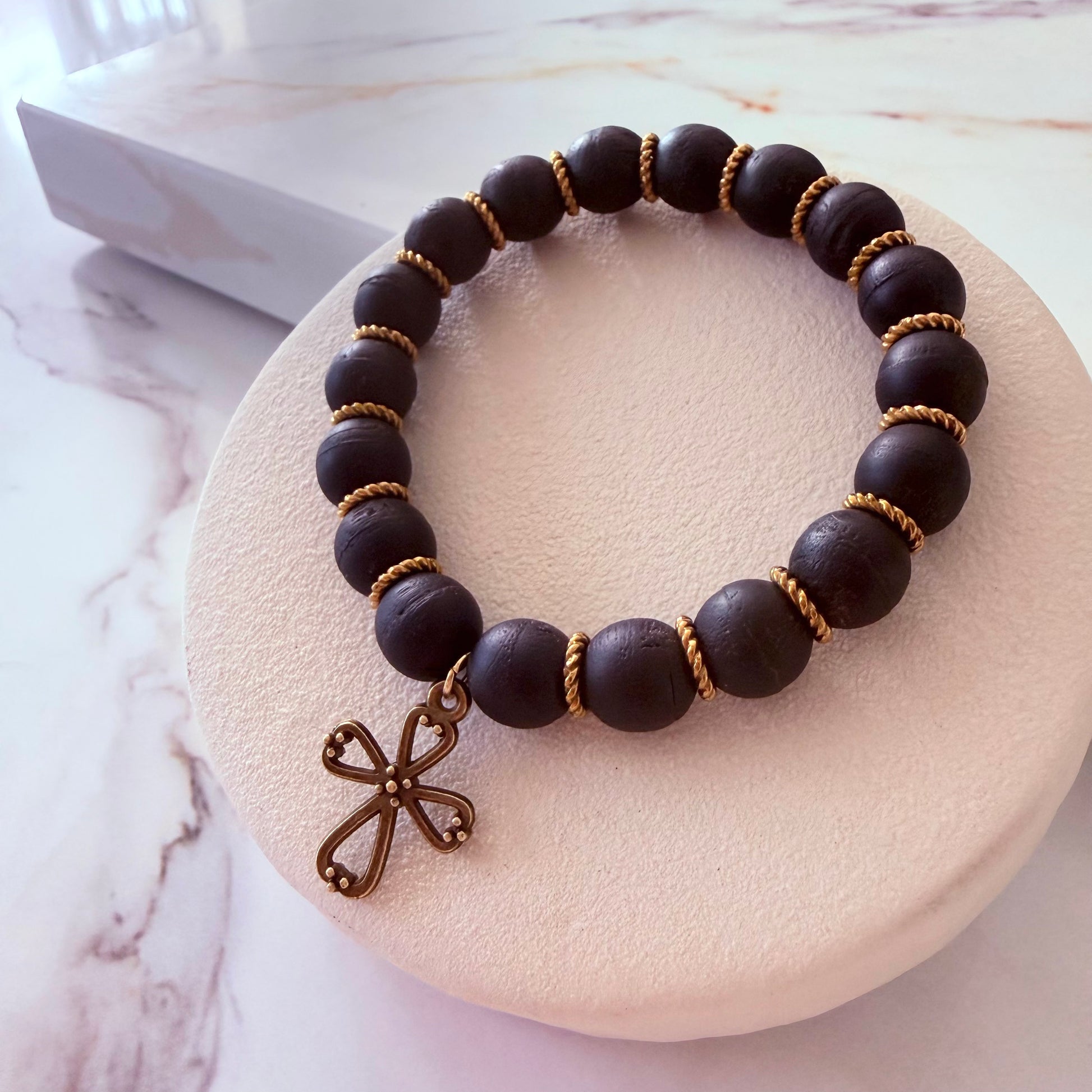 Black beaded bracelet with a bronze cross charm on a white stone surface.