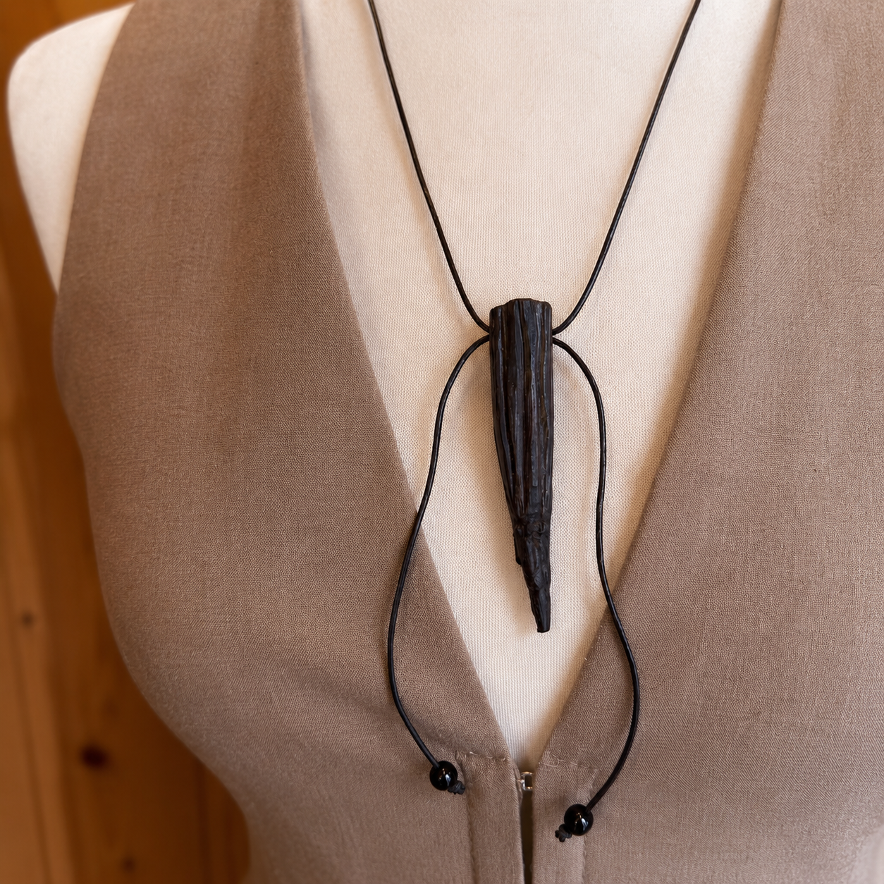 Necklace with a black pendant on a mannequin wearing a beige garment.