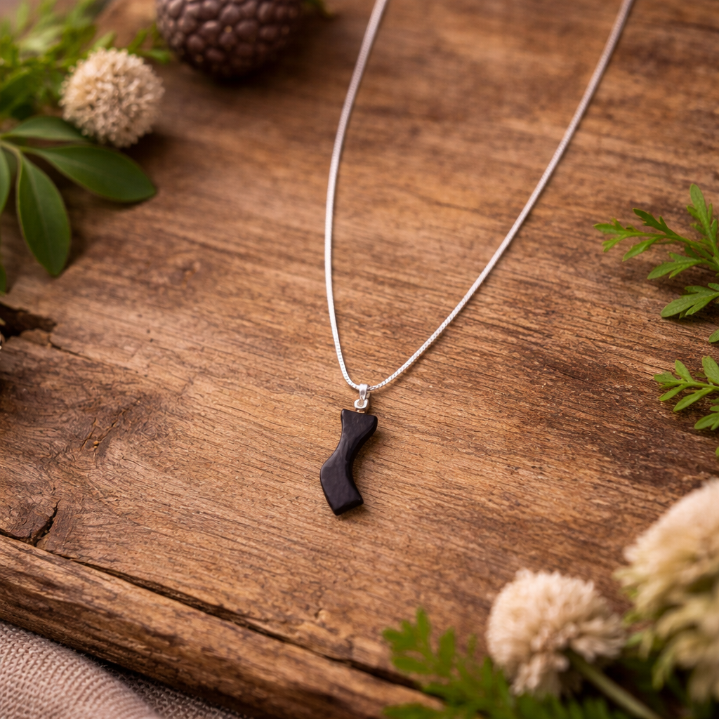 Necklace with a black pendant on a wooden surface with greenery