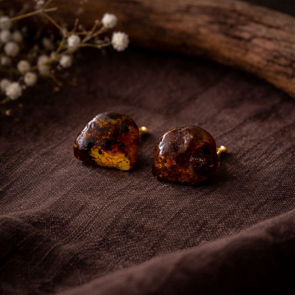 Pair of amber-colored earrings on a brown fabric background with white flowers.