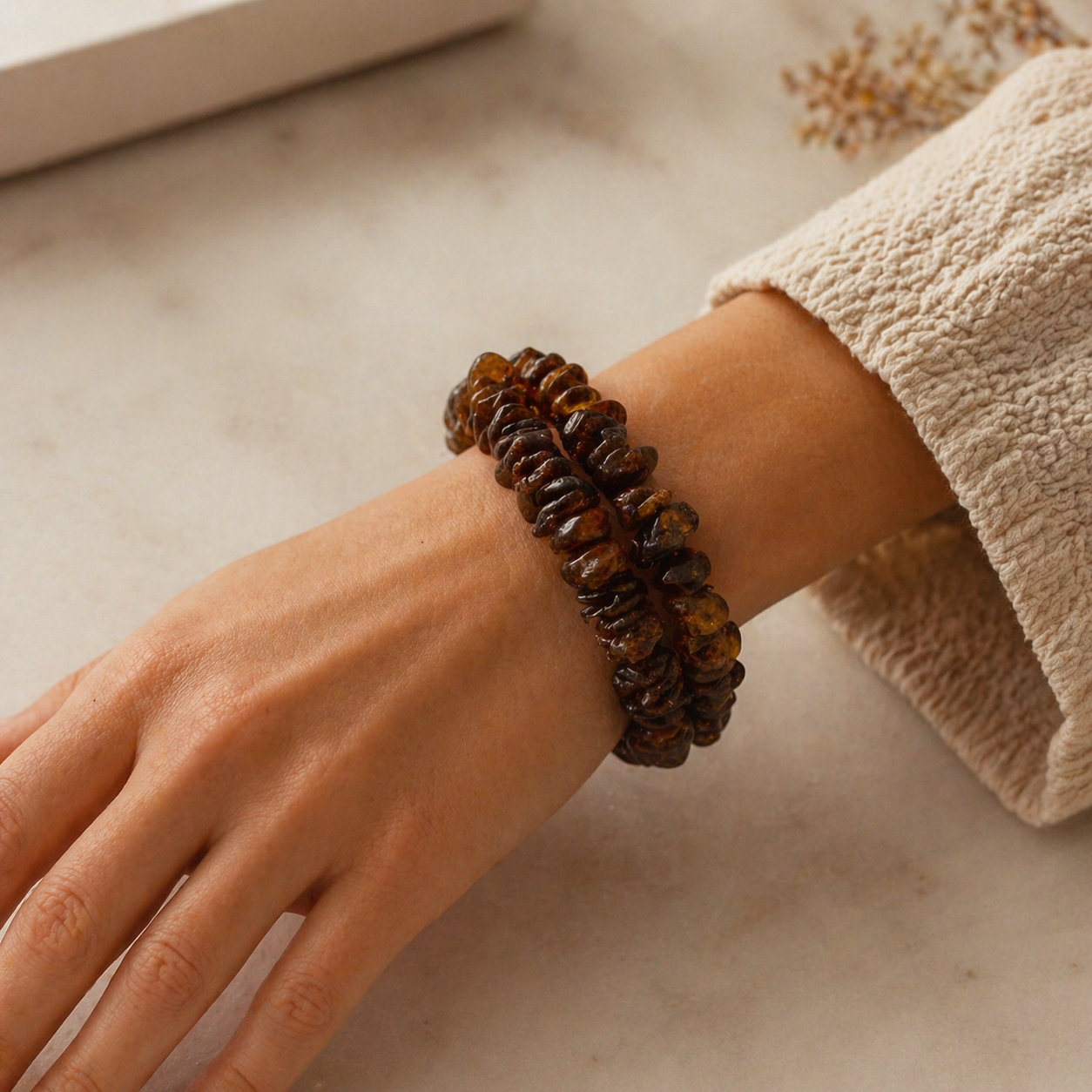 Hand wearing a brown beaded bracelet on a neutral background