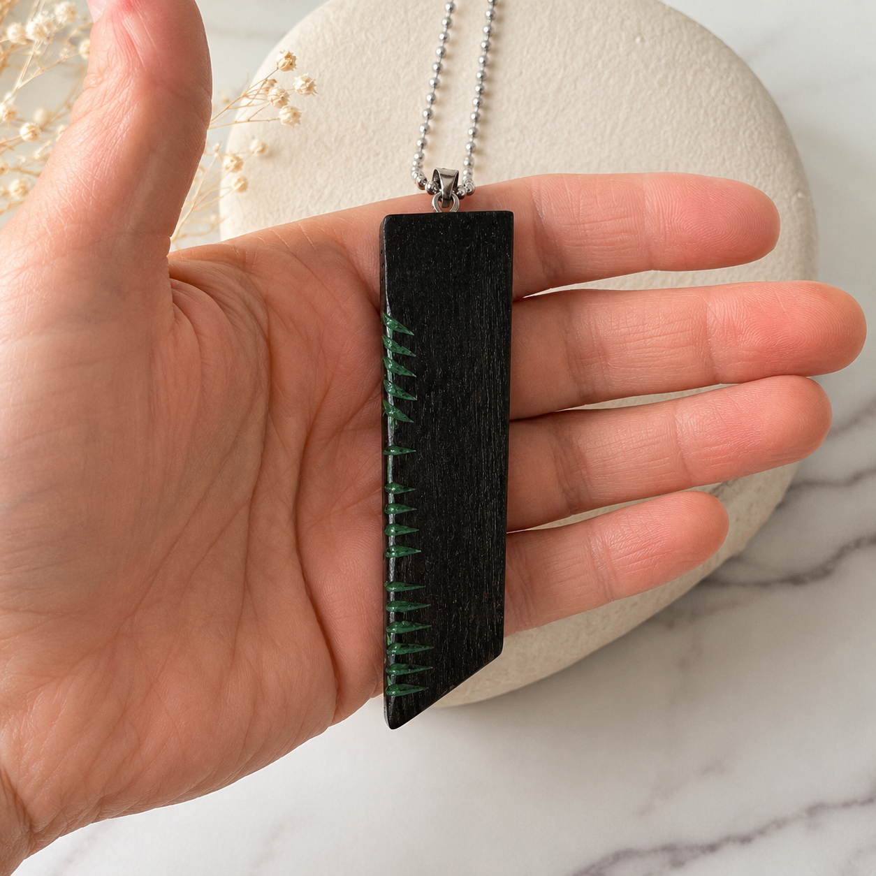 Hand holding a black pendant with green thread against a marble background