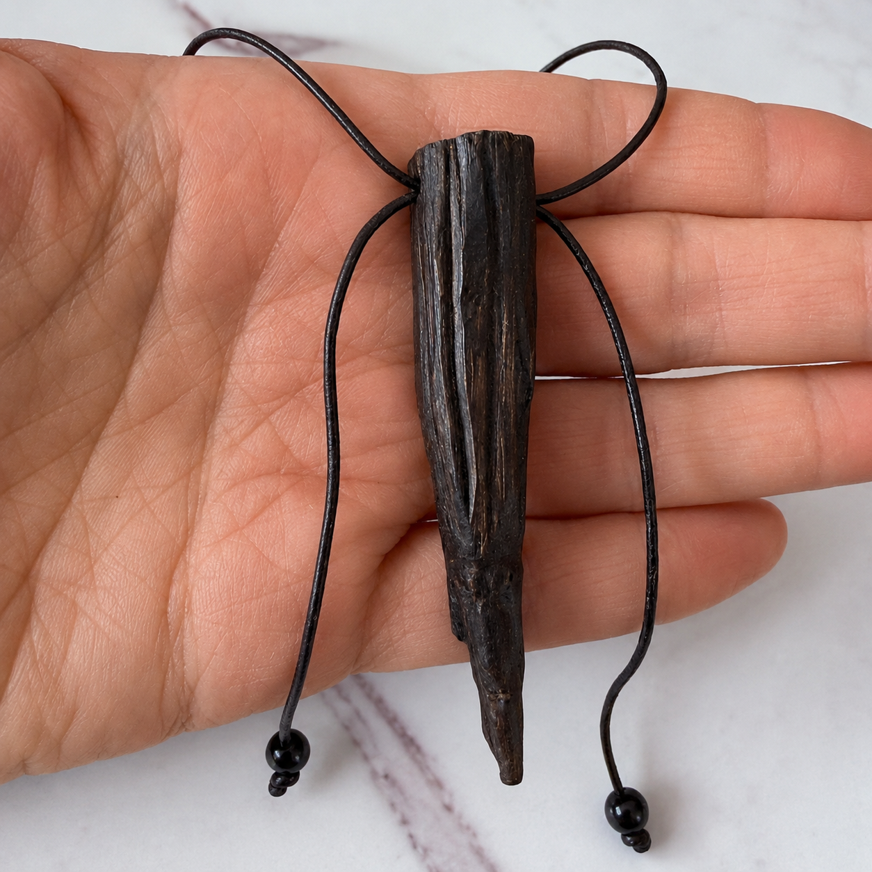 Wooden pendant with black strings held in a hand on a white background