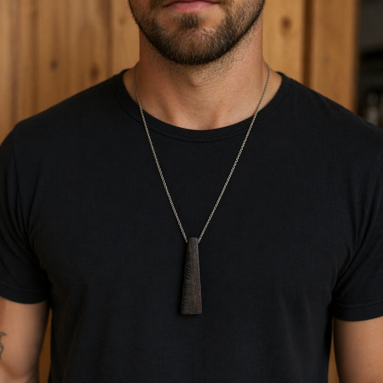 Man wearing a black t-shirt with a necklace featuring a pendant against a wooden background