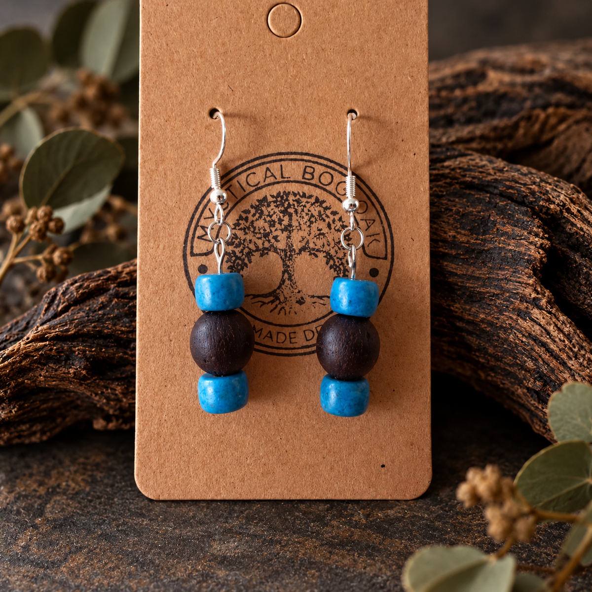 A pair of handmade dangle earrings displayed on a brown kraft card. The earrings feature bright blue beads, a dark brown wooden bead, and silver fishhook wires.
