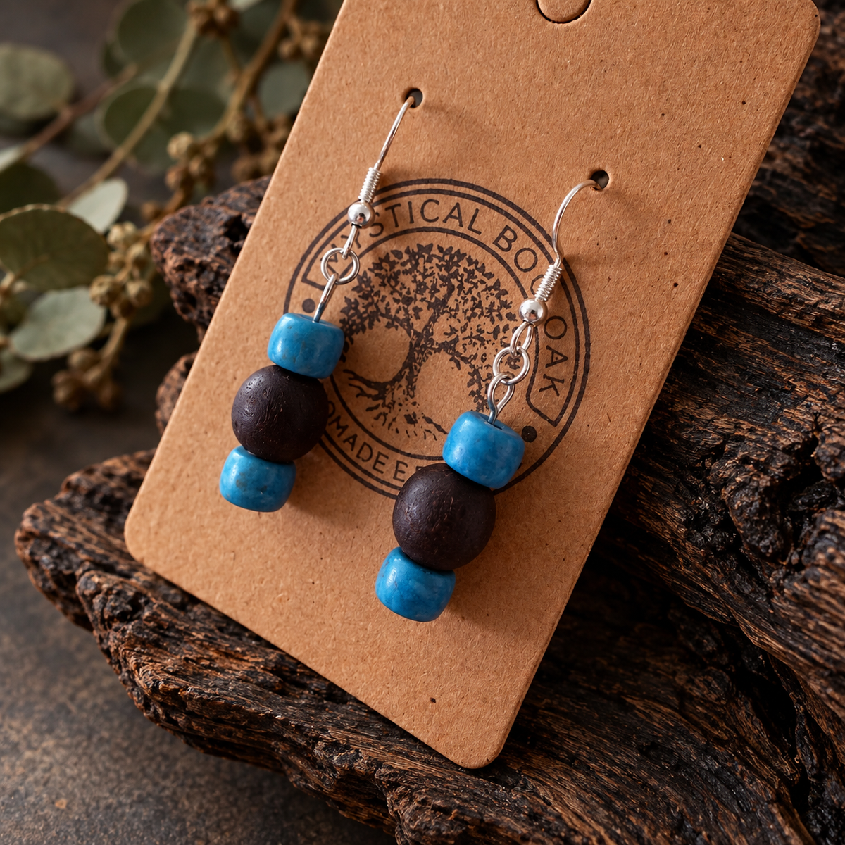 A pair of handmade dangle earrings displayed on a kraft paper backing card. The earrings feature bright turquoise blue beads, dark brown wooden beads, and silver-tone fishhook wires.