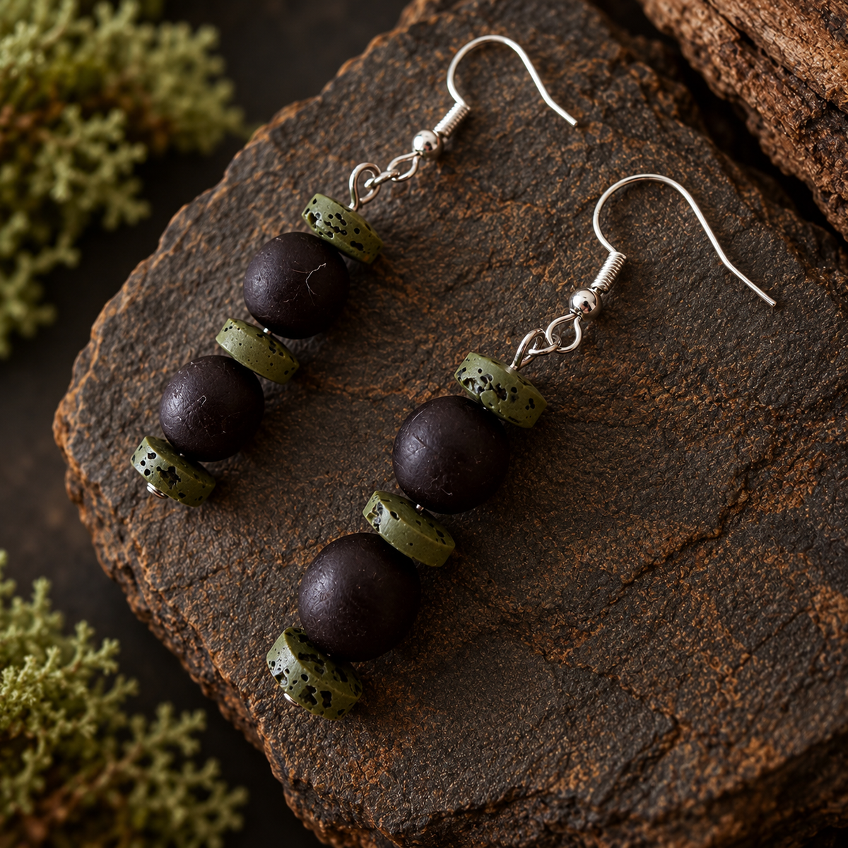 A pair of handmade dangle earrings with dark brown polished beads and textured olive-green spacer beads, displayed on a rustic dark wood surface.