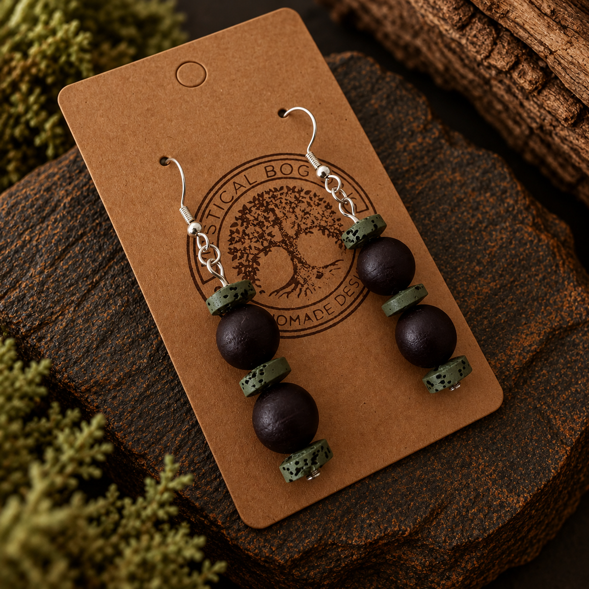 A pair of handmade dangle earrings displayed on a brown kraft card. The earrings feature dark brown wooden beads and textured green stone spacers, hanging from silver fishhook wires.