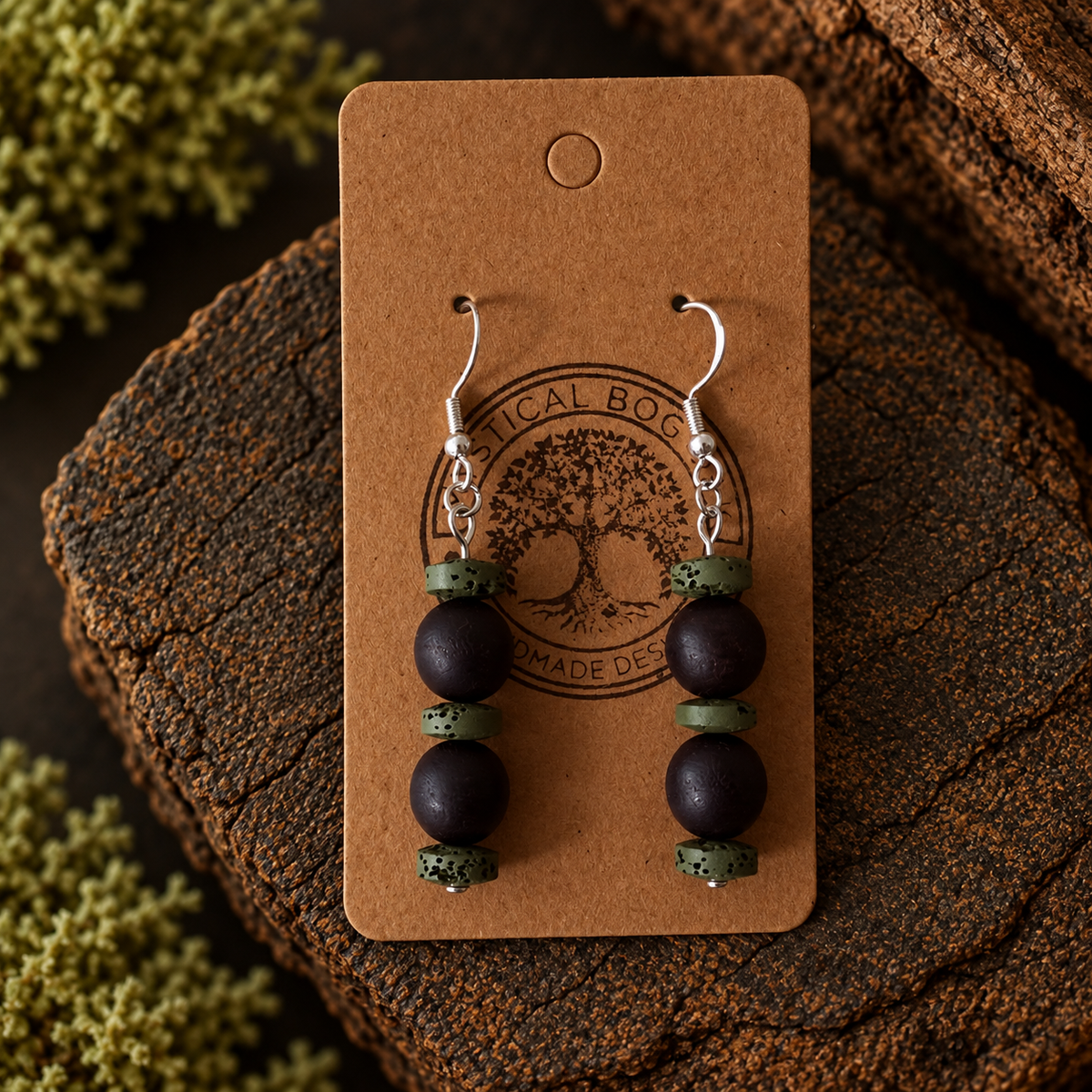 A pair of handmade dangle earrings displayed on a brown kraft card. The earrings feature three dark brown wooden beads and two small speckled sage green spacer beads, hanging from silver fishhook wires.