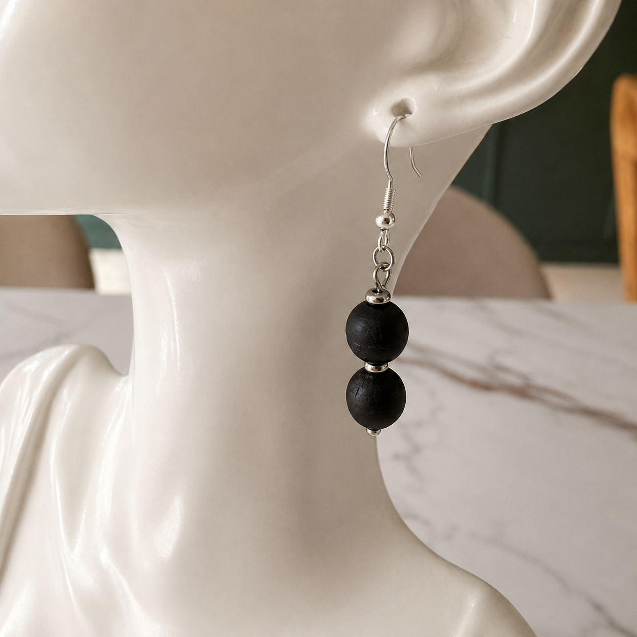 A single black beaded drop earring with silver-toned metal hardware, displayed on a white ceramic mannequin bust.