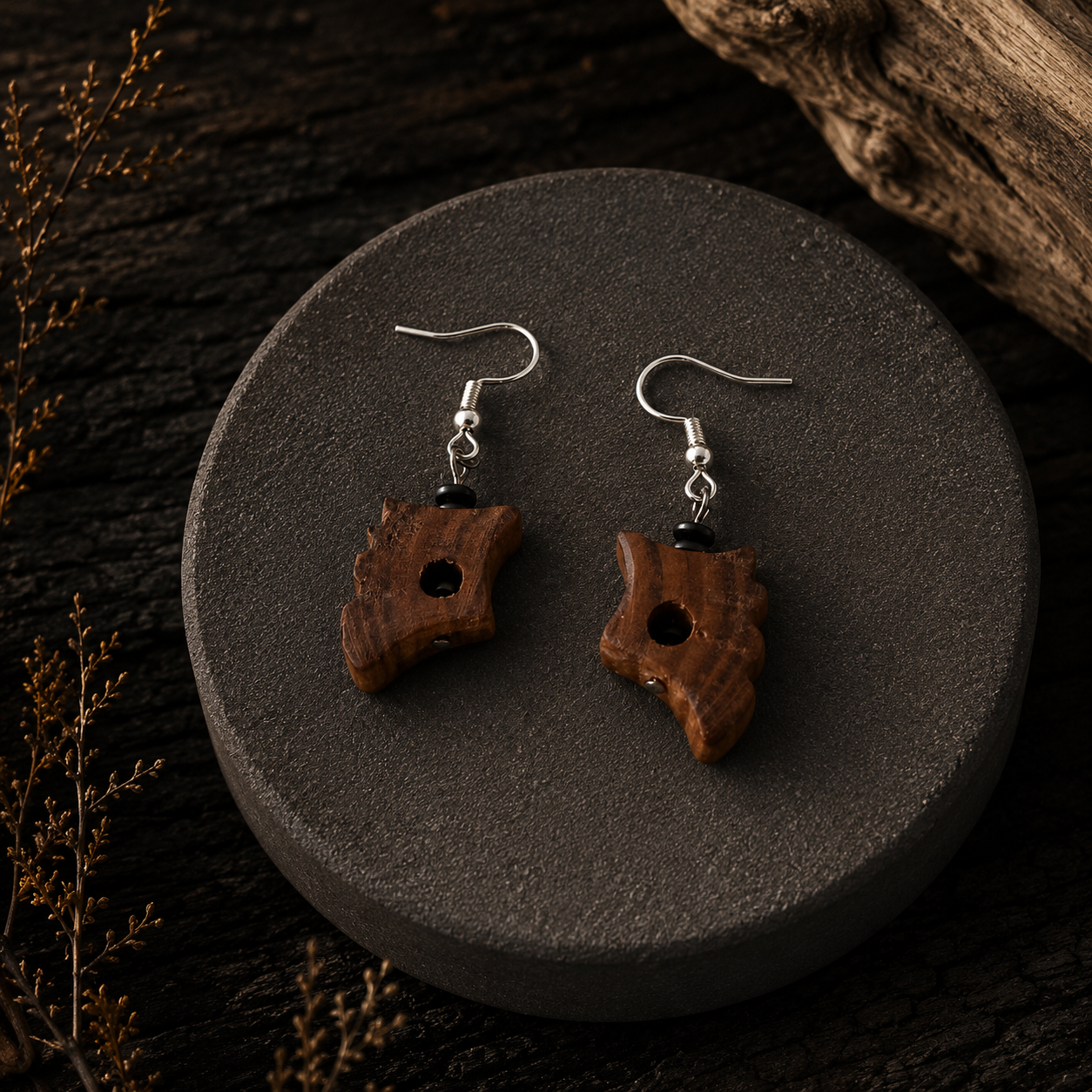 A pair of handmade wooden dangle earrings with silver fishhook wires, displayed on a round dark gray stone plate over a dark wood background.