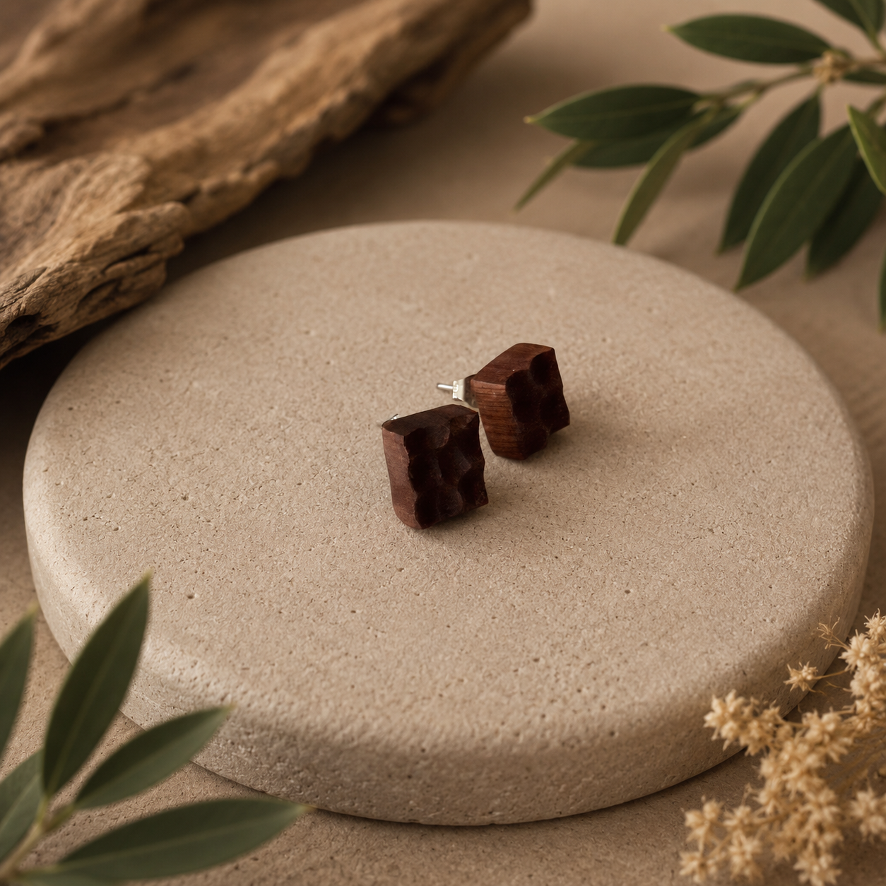 Wooden square earrings on a stone surface with natural elements.