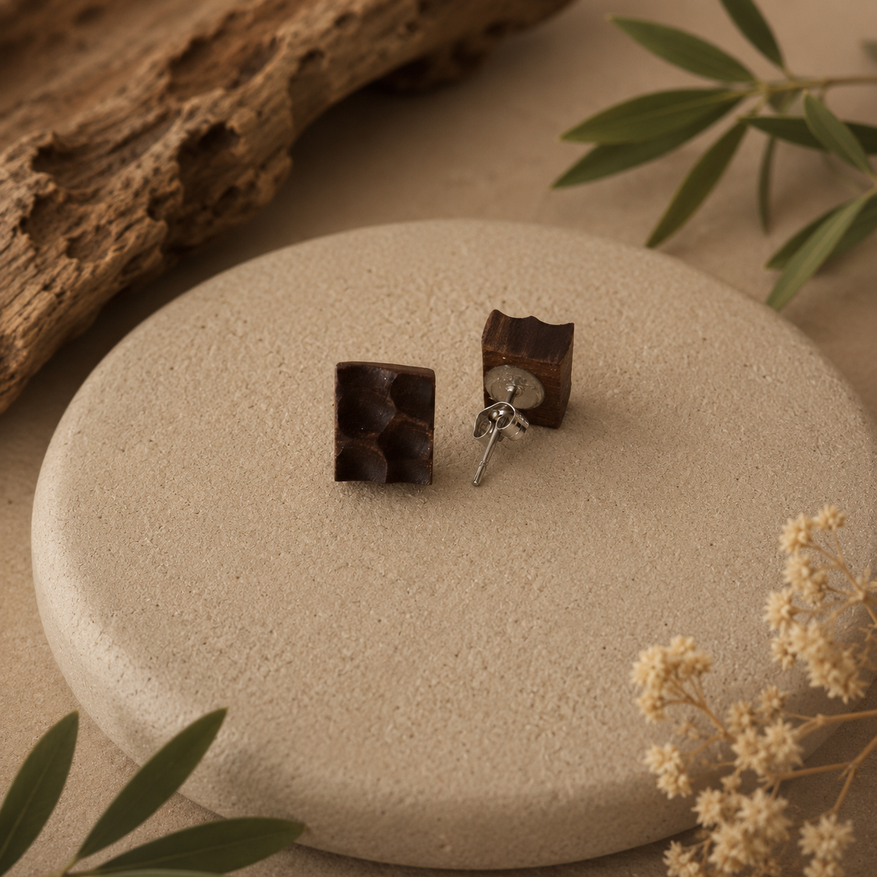 Wooden square earrings on a stone surface with natural elements.