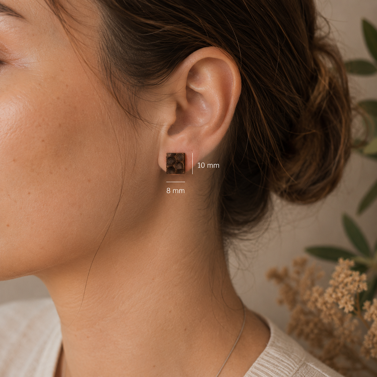 Close-up of a person wearing an earring with size measurement details, set against a neutral background.