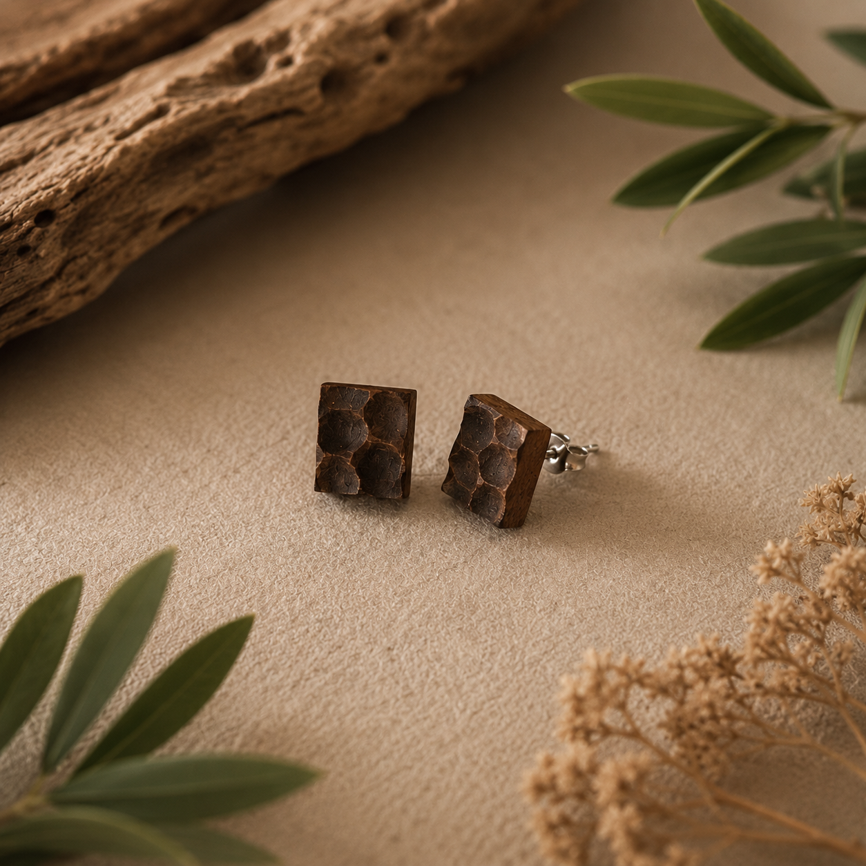 Brown square earrings on a beige surface with natural elements