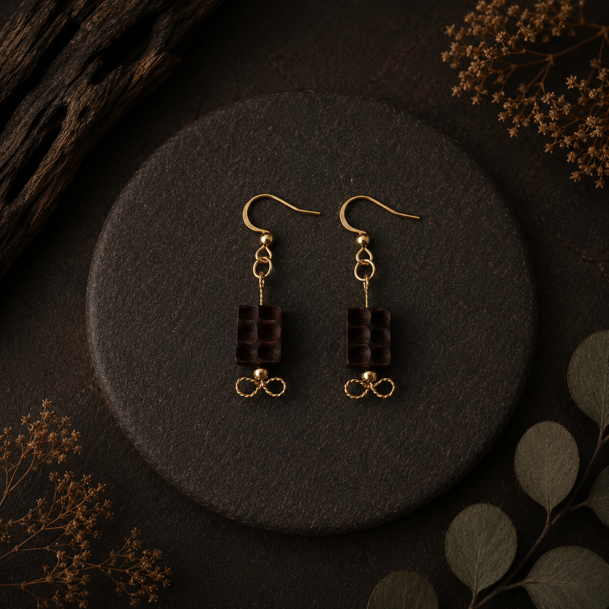 Pair of gold earrings with brown beads on a dark surface with dried plants.