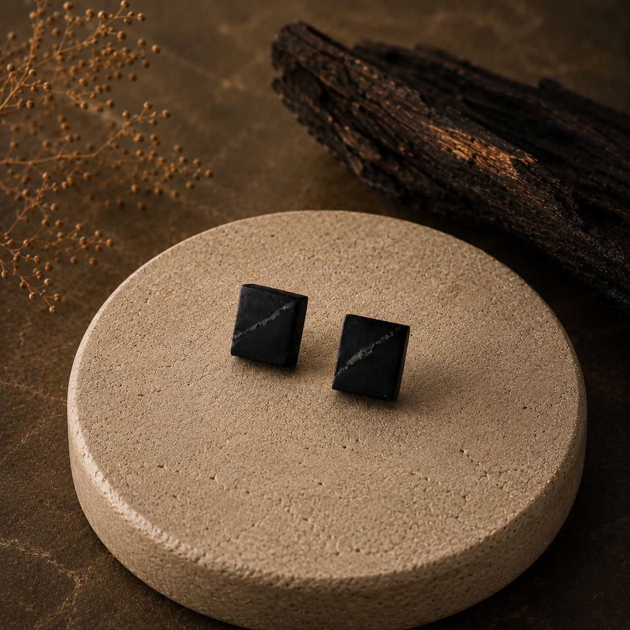 Black pyramid-shaped earrings on a beige stone surface with a brown background