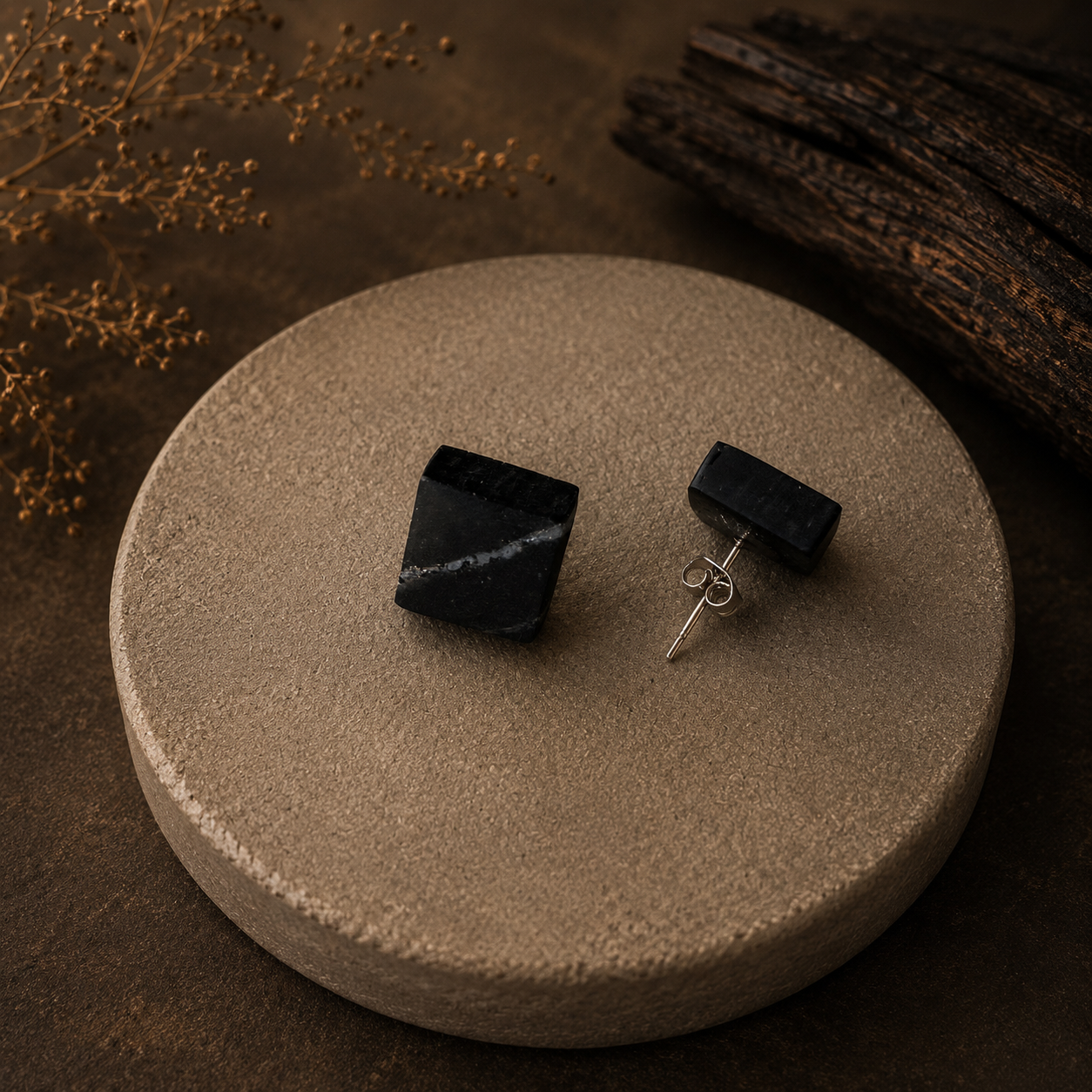 Black square earrings on a textured beige surface with a dark brown background