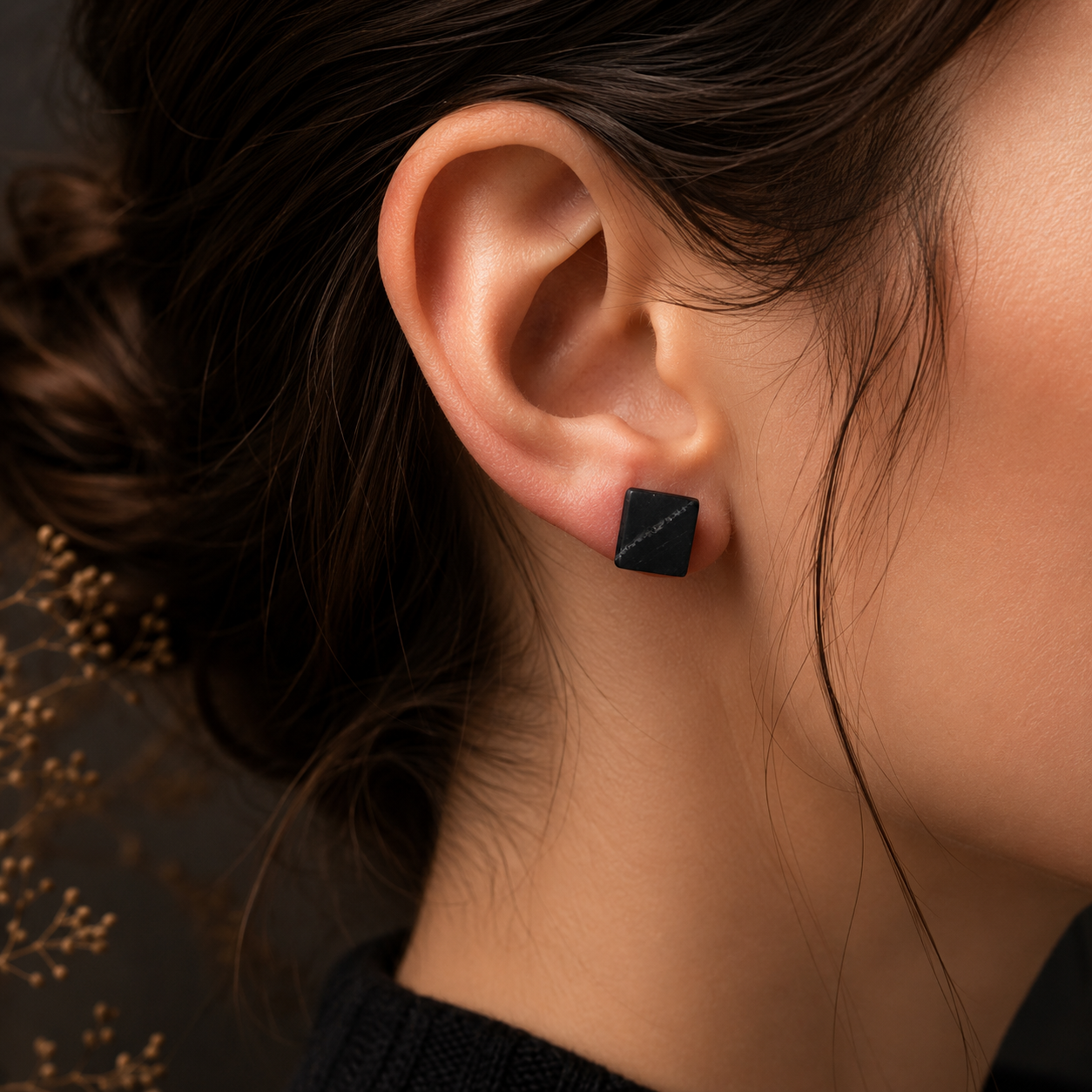 Close-up of an ear wearing a black square earring with blurred background