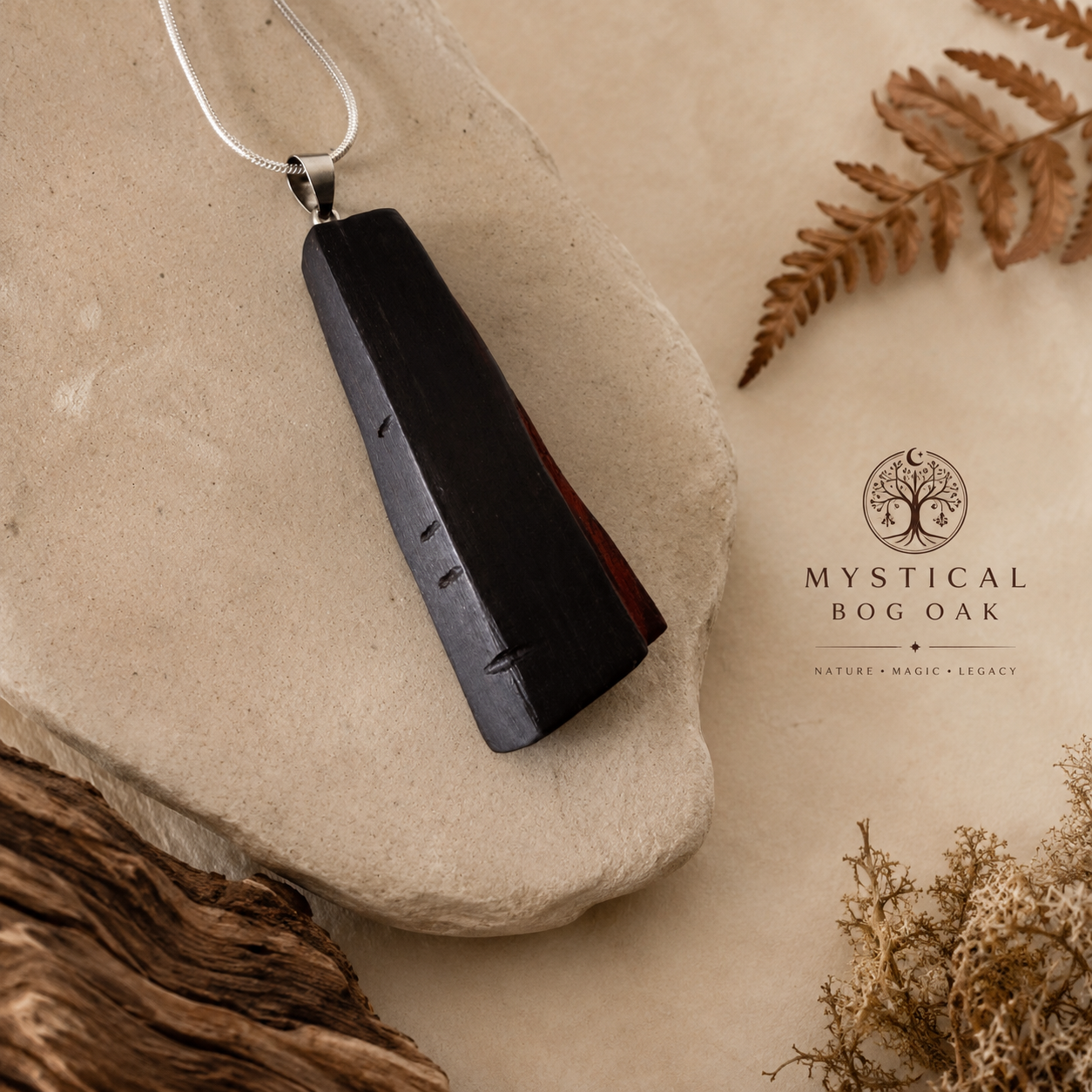 Black pendant on a stone with dried leaves and moss, featuring 'Mystical Bog Oak' brand.