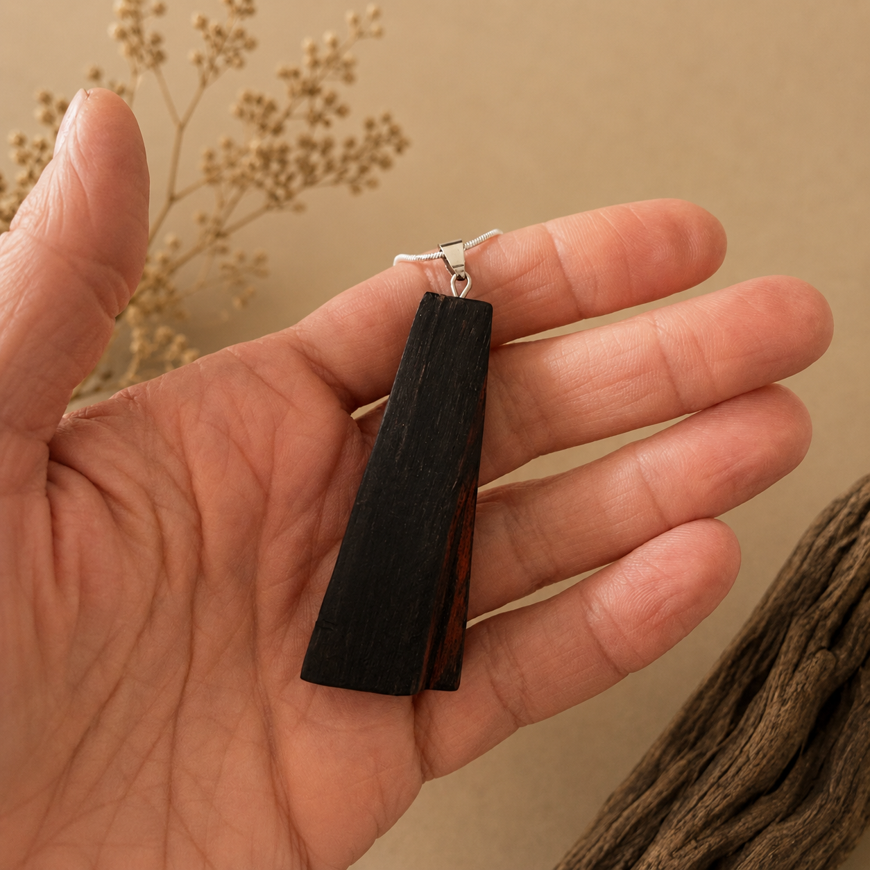Hand holding a black pendant with a beige background