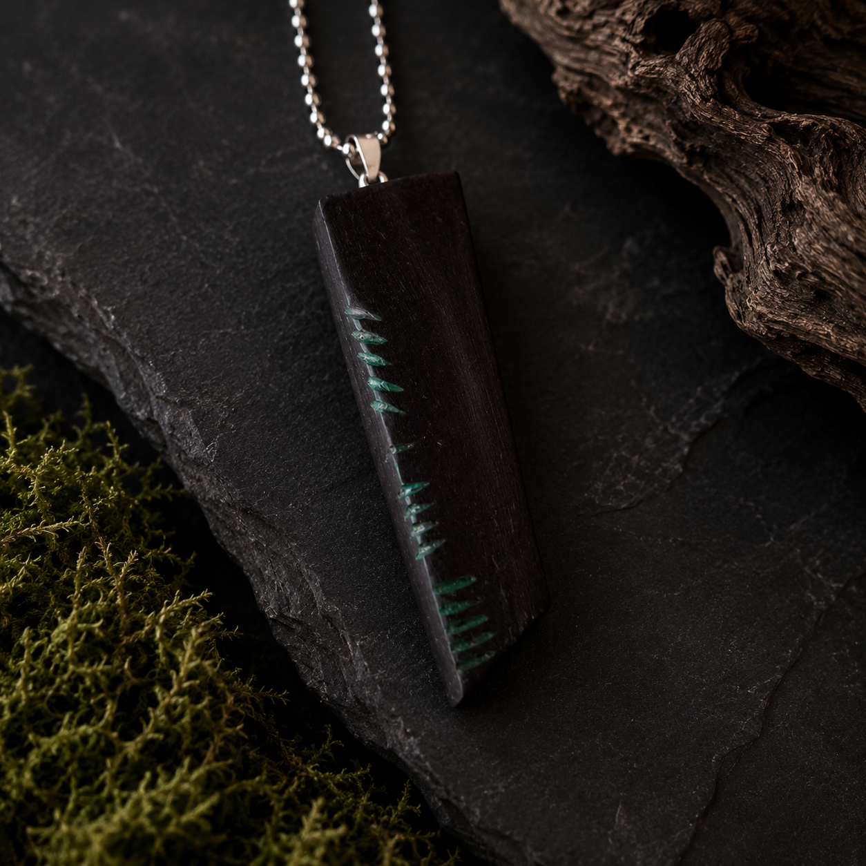Black pendant with green accents on a dark stone surface