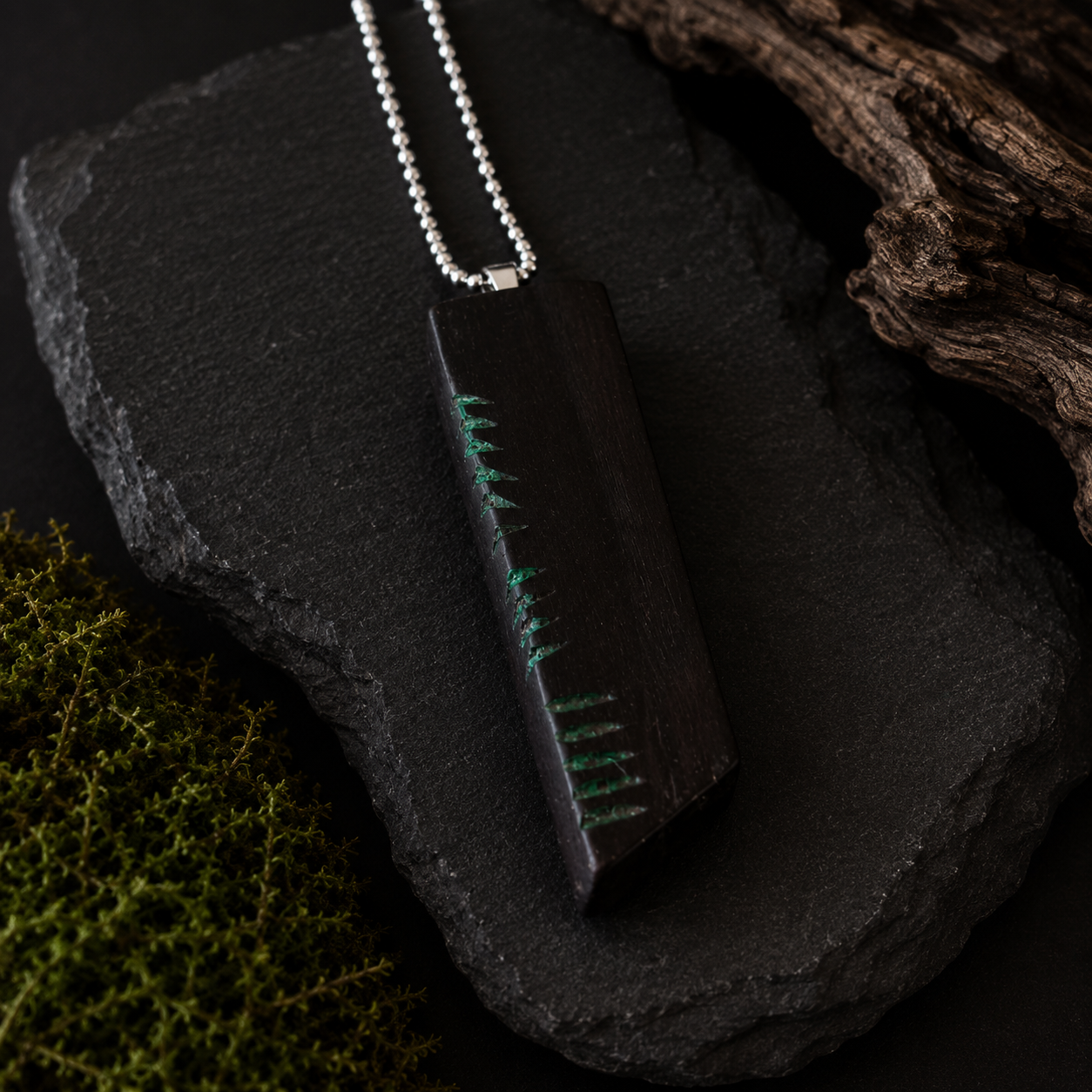 Wooden pendant with green embroidery on a dark stone surface