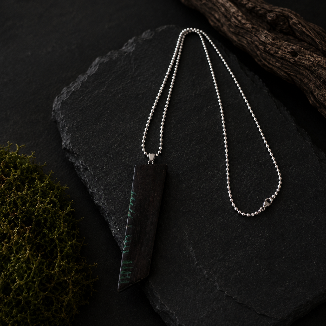 Silver necklace on a dark stone surface with natural elements