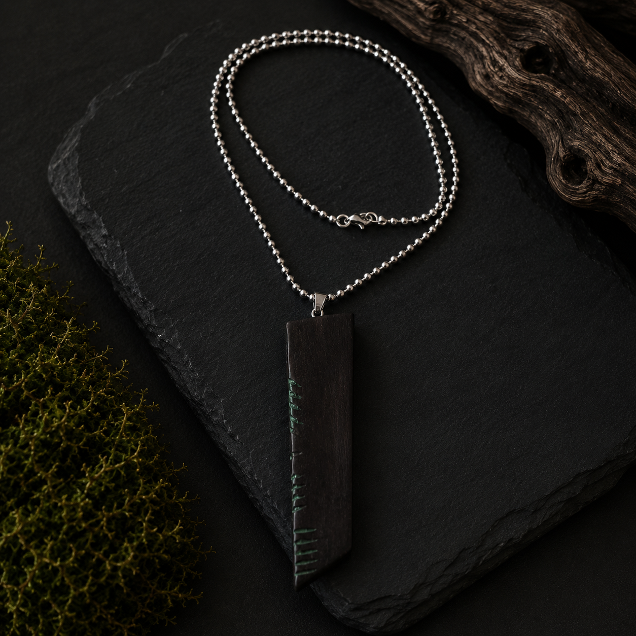 Silver necklace with a dark pendant on a black slate surface