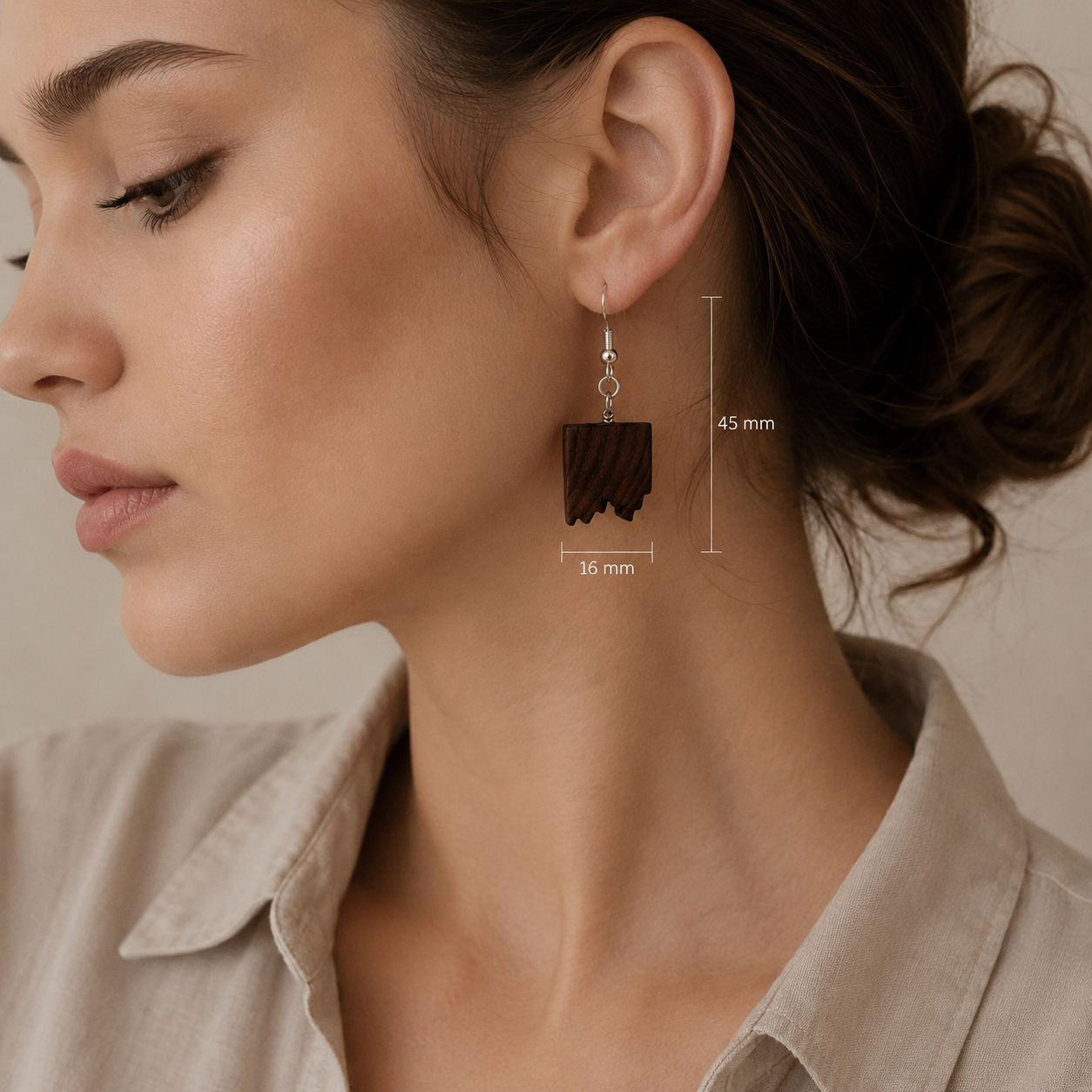 A close-up of a woman wearing a dark brown rectangular drop earring with a wood-grain texture. White measurement lines and text indicate the dimensions of the earring: 45 mm in height and 16 mm in width.