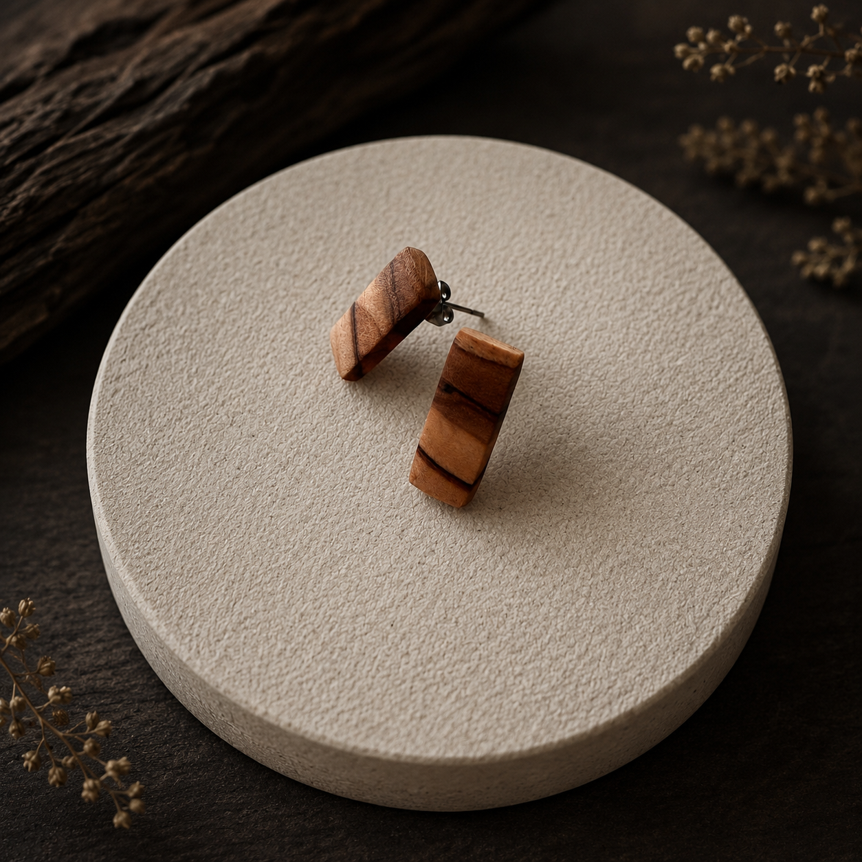 A pair of wooden stud earrings with a natural striped wood grain, displayed on a round textured beige ceramic plate against a dark wood background.