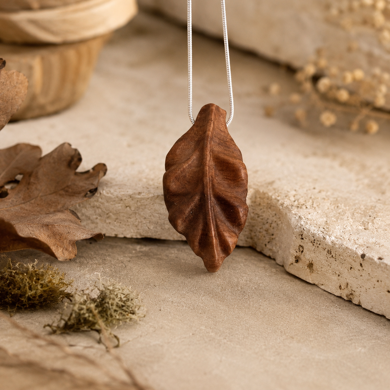 Brown leaf-shaped pendant on a chain, surrounded by natural elements on a stone surface.