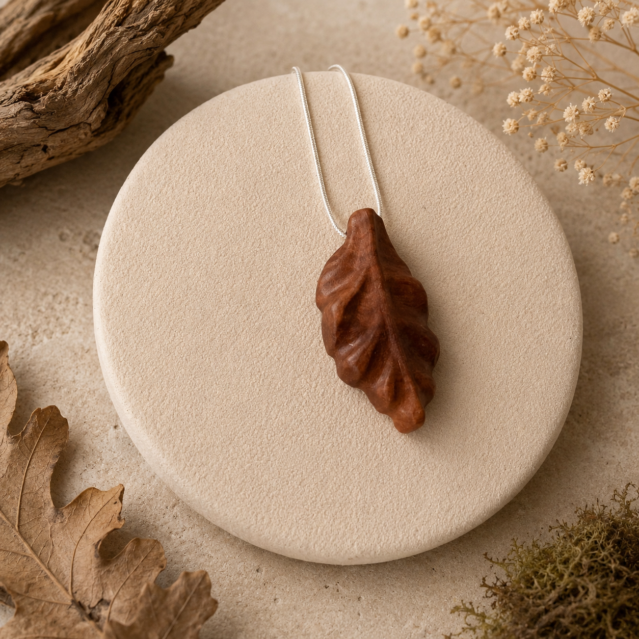 Brown leaf-shaped pendant on a white stone surface with natural elements around