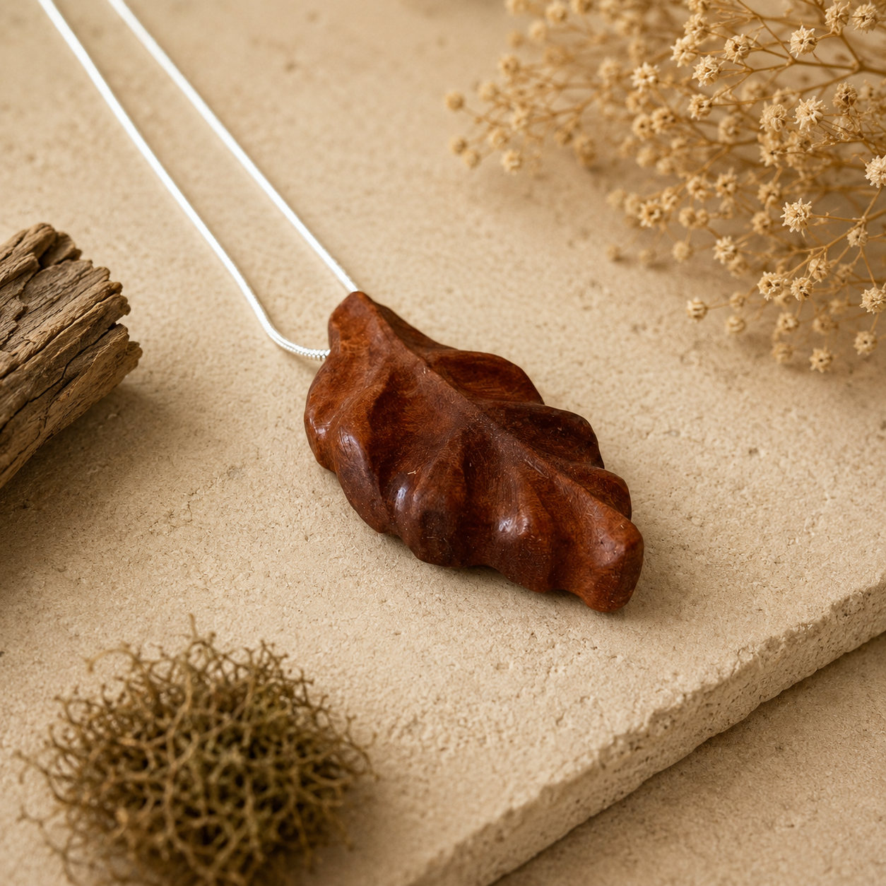 Brown leaf-shaped pendant on a white cord with natural elements on a beige surface