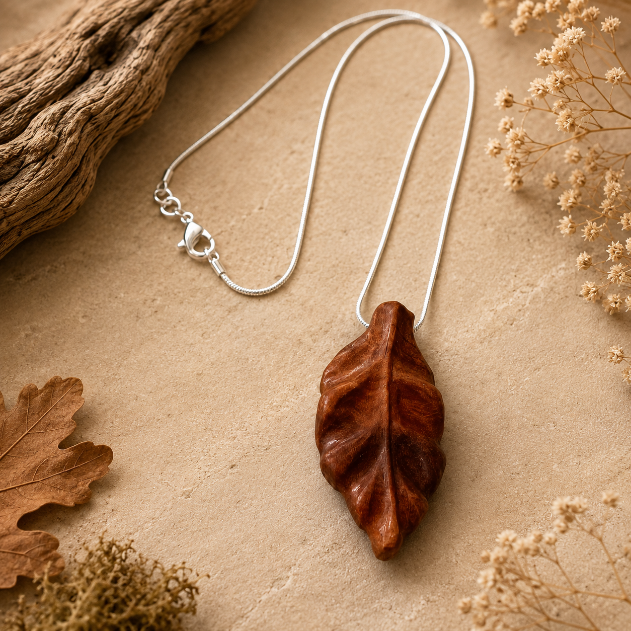 Wooden leaf pendant on a silver chain with natural elements on a beige background