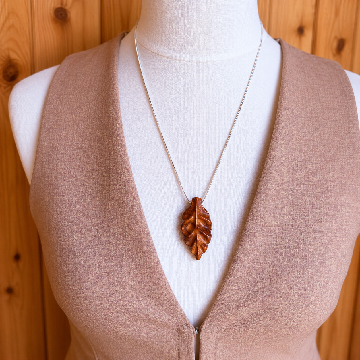 Mannequin wearing a brown vest with a necklace featuring a leaf pendant against a wooden background
