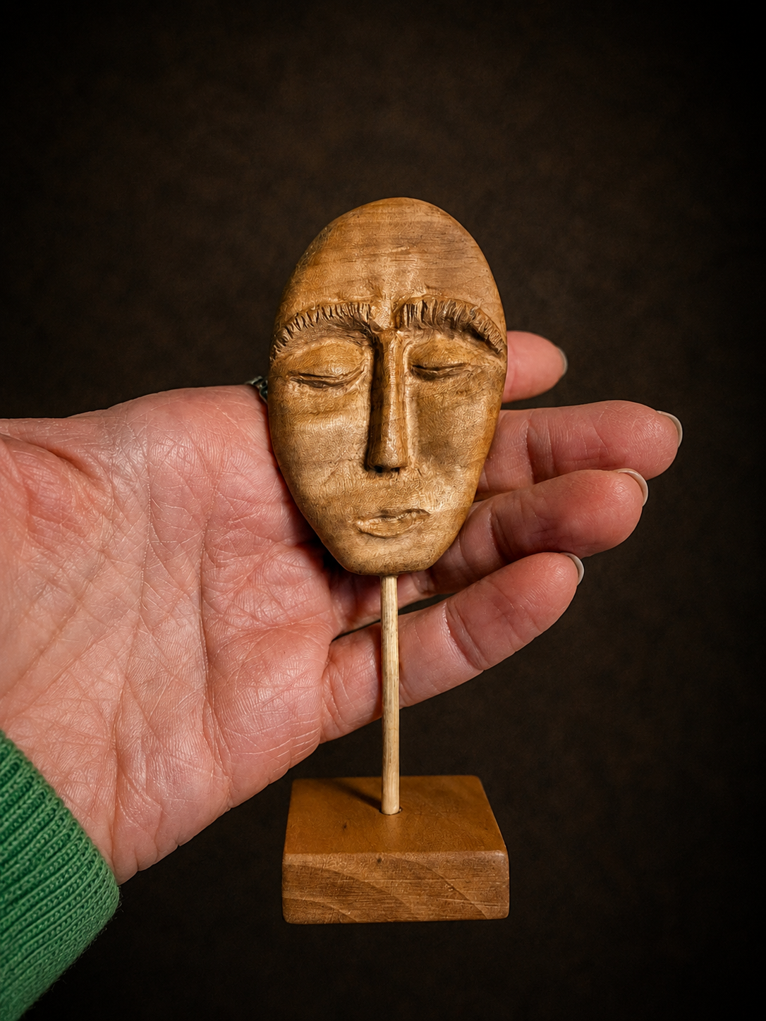 Wooden mask on a stick held in a hand against a dark background